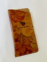 Portalentes Aruba de cuero con estampado floreado en tonos marrones y anaranjados, con costuras blancas a la vista y logo grabado de la marca.