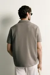 Remera polo regular fit de color gris oscuro, confeccionada en tejido de algodón con textura de rayas verticales. Cuenta con cuello solapa, cierre frontal con botones y mangas cortas con terminación en rib.
