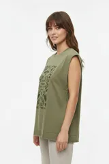 Musculosa color crudo con estampado frontal de paisaje montañoso y texto "EXPLORING Outlands", corte holgado y aberturas laterales en el ruedo.