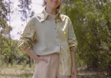 Camisa blanca con estampado de hojas en tonos beige y verde, cuello camisero, mangas largas con lazos en los puños y botones de madera.