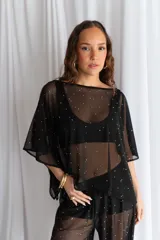 Blusa de tul negro translúcido con aplicaciones de perlas blancas dispersas, de corte amplio y mangas murciélago holgadas.