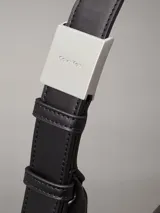 Cartera tipo hobo de piel sintética negra, con silueta fluida y correa ajustable con herrajes metálicos. Presenta cierre de cremallera principal y logo Calvin Klein grabado en la parte delantera.