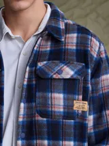 Sobrecamisa de tejido polar con estampado abstracto en tonos rojizos y azul marino. Presenta cuello clásico, cierre frontal con botones a presión, dos bolsillos frontales con solapa en el pecho y un parche decorativo.