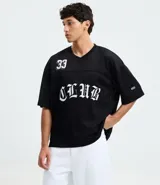 Remera masculina negra de estilo sportcore, modelo boxy con cuello en V y manga corta. Presenta textura "furadinha" (perforada), estampado numeral "33" en el hombro y "CLUB" en el pecho, ambos en blanco con tipografía gótica.