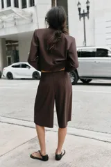 Bermuda de tiro alto en color marrón chocolate, con diseño de corte recto y largo por encima de la rodilla. Presenta pinzas delanteras, bolsillos laterales y cierre frontal con cremallera, botón y gancho.