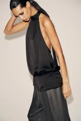 Top negro de tejido satinado con cuello halter y lazada. Cierre lateral con cremallera oculta.