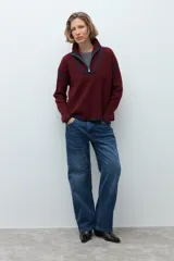 Sweater de punto color crudo con cuello alto y cierre frontal parcial. Presenta detalles de vivos en color marrón en el cuello, hombros y ruedo, con diseño de manga larga.