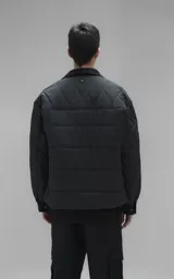 Campera tipo sobrecamisa de diseño oversize, confeccionada en microfibra opaca con patrón matelaseado geométrico. Presenta cuello, puños, cartera central y ruedo en gabardina de algodón, con cierre frontal mediante broches a presión. El diseño del ruedo simula una prenda superpuesta.