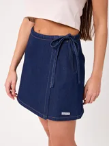 Falda corta de jean tipo pareo, con diseño cruzado para atar con tiras laterales, costuras pespunteadas a contratono y calce holgado.