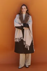 Ruana de tejido de punto en color beige, con cuello de piel sintética y terminaciones con flecos en el ruedo.