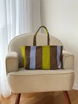 Cartera tipo tote bag de diseño amplio y moderno, confeccionada en cuero con franjas verticales en colores marrón, verde y celeste. Cuenta con doble asa de hombro y cierre superior.