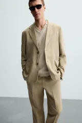 Blazer color beige de corte relaxed fit, confeccionada en tejido con viscosa. Tiene cuello con solapas de muesca, manga larga con puño abotonado, bolsillos frontales de plastrón, medio forro interior, aberturas en la espalda y cierre frontal con botones. Presenta un efecto lavado.