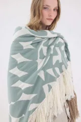 Ruana de punto triangular tejida en lambswool, con diseño geométrico en tonos tostado, blanco y negro, terminada con flecos en los bordes.