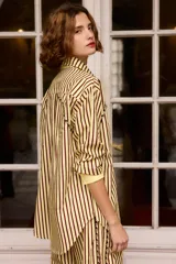 Camisa de algodón con diseño a rayas verticales en tonos oscuros, cuello clásico y cierre frontal con botones. Presenta detalles bordados en color amarillo a lo largo de las costuras laterales y en la parte superior delantera.