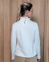 Polera de manga larga color blanco, confeccionada en algodón, con cuello alto tipo tortuga y detalles de volados en el cuello y en los puños.