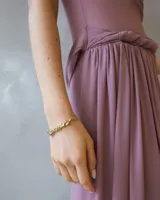 Vestido largo color malva con escote barco, cuerpo ajustado y falda fluida con detalle de drapeado y fruncido en la cintura.
