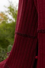 Buzo reversible de tejido fino con sutil brillo, color bordó, con cuello bote y mangas largas acampanadas. Presenta costuras decorativas horizontales y botones en forma de flor a los costados.