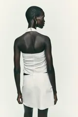 Top negro con cuello halter, escote pico y espalda descubierta. Presenta detalle de frunces laterales y cierre frontal con botones.