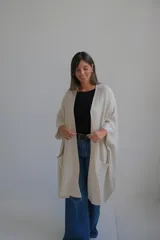 Poncho abierto de tejido de punto color crudo, con mangas tres cuartos y bolsillos frontales aplicados.