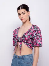 Top estampado con flores rosas, hojas verdes y líneas negras, de manga corta abullonada con nudo en el escote.