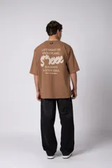 Remera oversize de algodón color beige, de manga corta y cuello redondo, con pequeño estampado frontal de la marca en tono bordó.