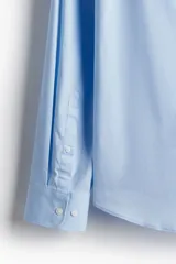Camisa de manga larga color celeste claro, con cuello italiano y tapeta lisa con botones blancos. Presenta un corte ajustado (slim fit) y bajo redondeado.