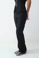 Pantalón negro de tiro medio con corte flare, confeccionado en tejido elasticado. Presenta una costura central y una pequeña abertura en el ruedo. Cierre frontal oculto.