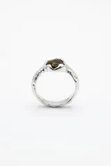 Anillo de metal plateado con diseño irregular y texturizado tipo machacado, con una piedra central en tonos marrones.