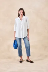 Camisa de corte holgado y fluido, color blanco, con cuello clásico, cierre frontal de botones y mangas tres cuartos con puños rectos.