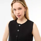 Chaleco sin mangas de color negro, con cuello redondo y cierre frontal mediante botones. Presenta un diseño corto con una abertura en la parte inferior.