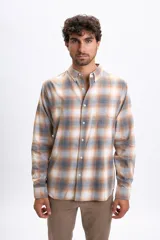 Camisa de manga larga con estampado de cuadros en tonos gris, beige y blanco. Presenta cuello abotonado, cierre frontal con botones y un bolsillo en el pecho.