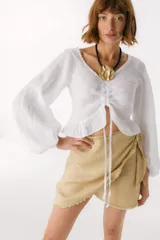 Top de lino italiano color blanco, con escote en V, mangas largas estilo globo y detalle de jareta frontal ajustable con volado en el ruedo.