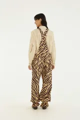 Jardinero largo confeccionado en denim con estampado animal print de cebra en tonos beige y marrón. Presenta tiradores regulables, cierre frontal con botones, bolsillos laterales y piernas amplias con ajuste en los tobillos.