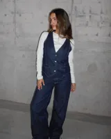 Chaleco de jean azul con broches metálicos y detalle de hebilla en la espalda.