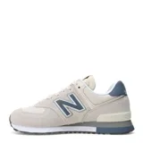 Championes urbanos New Balance modelo 574, color beige con detalles en azul marino y gris. Confeccionados en una combinación de gamuza y malla, cuentan con el logo N característico en los laterales, entresuela con tecnología ENCAP para mayor estabilidad y suela de goma.