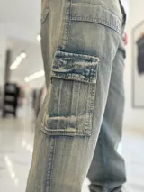 Pantalón cargo de jean azul claro, con bolsillos laterales tipo cargo en las piernas y bolsillos frontales aplicados, de corte ancho y holgado.