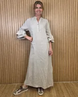 Vestido largo estilo túnica color beige, con escote en V y botones frontales a medio cuerpo, de corte recto y mangas tres cuartos terminadas en volados escalonados.