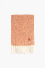 Bufanda de tejido suave con textura jaspeada en color naranja y detalle de flecos largos en color blanco en los extremos. Incluye una pequeña etiqueta de cuero sintético con logo grabado.