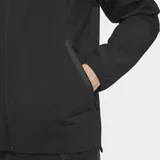 Campera deportiva Adidas del Real Madrid, color negro, con cierre frontal, capucha y corte entallado. Presenta el logo de Adidas y el escudo del club en tono sobre tono en el pecho.