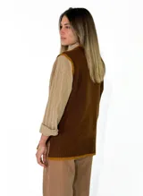 Chaleco de punto color marrón con detalles en color mostaza en el cuello, sisas y ruedo. Presenta un diseño de corte recto y un pequeño aplique decorativo en forma de flor en la parte inferior.