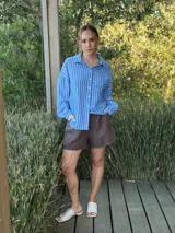 Camisa celeste con rayas verticales blancas, de manga larga, cuello camisero y cierre frontal con botones.