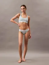 Bralette deportivo de algodón con diseño de espalda cruzada, sin forro ni relleno. Presenta una banda elástica inferior con el logo de la marca estampado.