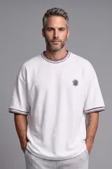 Remera blanca de manga corta con ribetes a rayas marrones en cuello y puños, corte oversize y pequeño bordado circular en el pecho.