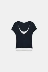 Camiseta de manga corta y corte slim fit, con cuello redondo y cierre frontal de botones a presión. Presenta un diseño de efecto doble capa a contraste con una camiseta interior blanca visible en el cuello y el ruedo.