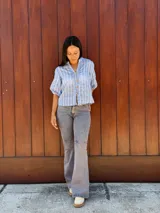 Camisa de corte recto y calce holgado, confeccionada en tela liviana color celeste con estampado de rayas verticales blancas con detalles de hojas. Presenta cuello en V, cierre frontal con botones de madera y mangas tres cuartos con terminación elástica.