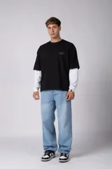 Remera de manga larga con diseño de doble capa, que combina una remera de manga corta color marrón moka con una base de manga larga blanca. Presenta un pequeño logo gráfico en el pecho y un detalle de etiqueta en el puño.