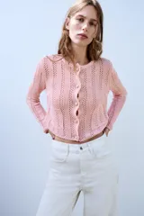Chaqueta de punto pointelle en color rosado, con cuello redondo, manga larga y bolsillos delanteros de parche. Cuenta con cierre frontal de botones claros.