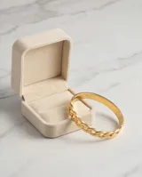 Esclava de acero con baño de oro, con diseño de eslabones tipo cadena en la parte superior y una cadena fina adicional integrada.