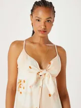 Musculosa tipo túnica de largo midi, con diseño estampado de flores en tonos claros y detalles en naranja. Presenta un escote en V con detalle de nudo frontal y breteles finos.