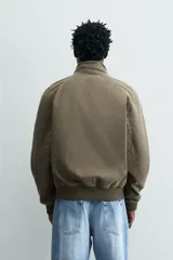 Cazadora de corte relajado color verde militar, con cuello subido, cierre frontal con cremallera y bolsillos laterales con solapa. Presenta puños y ruedo con acabado en rib.
